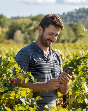 Imagem de um homem usando um smartphone em meio a uma plantação verde