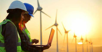 Dois técnicos em elétrica usando um notebook próximos a uma estação de energia eólica